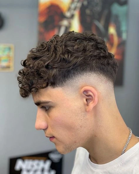 Corte de pelo low fade para cabello rizado, manteniendo los rizos naturales en la parte superior mientras los lados tienen un degradado bien definido.