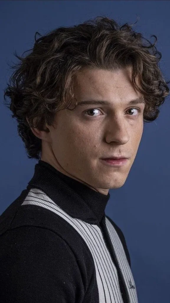 Corte de pelo con la parte superior rizada y los lados degradados bajos al estilo Tom Holland, para un look moderno y bien estructurado.